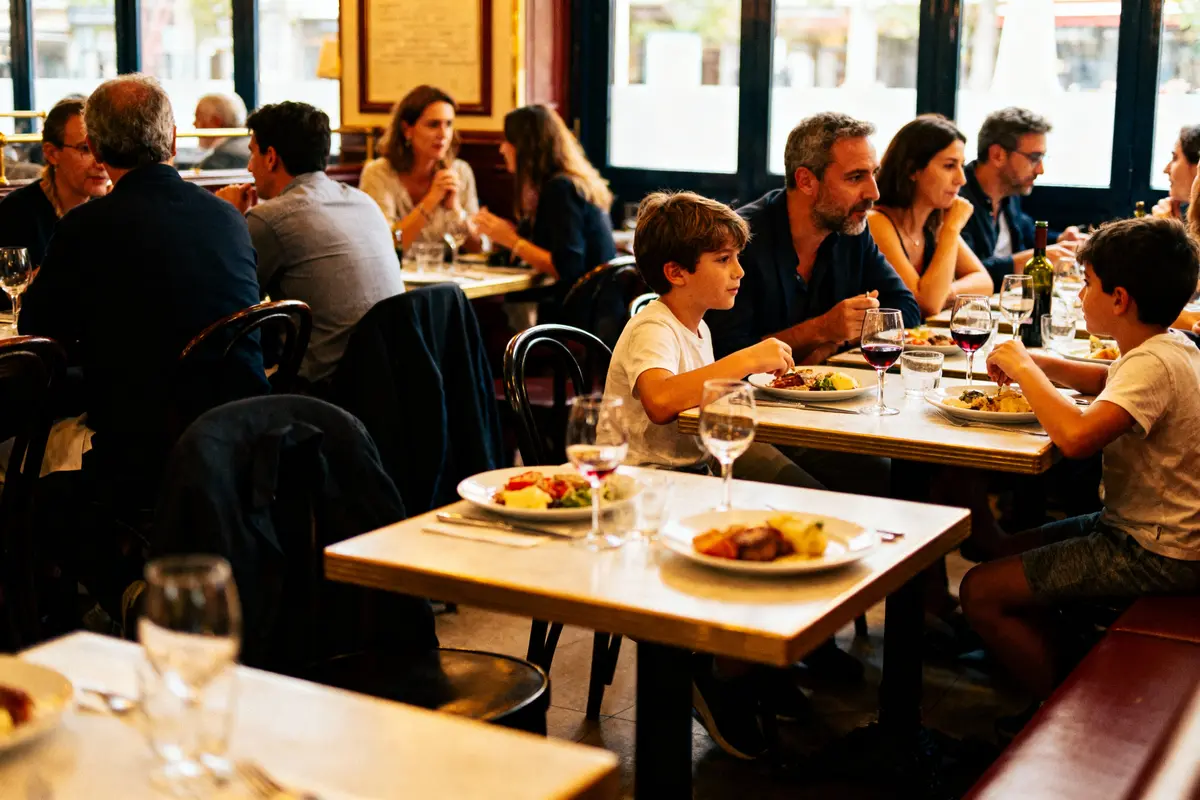 Des personnes dînent dans un restaurant animé, discutant et partageant un repas sur des tables en bois.