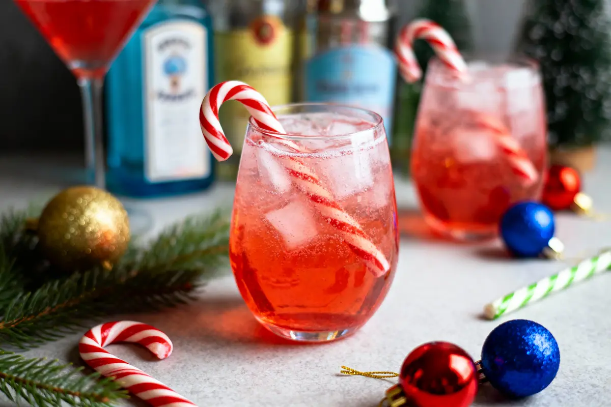 Verres de cocktail rouge avec cannes de Noël, décorés de boules colorées et branches de sapin.
