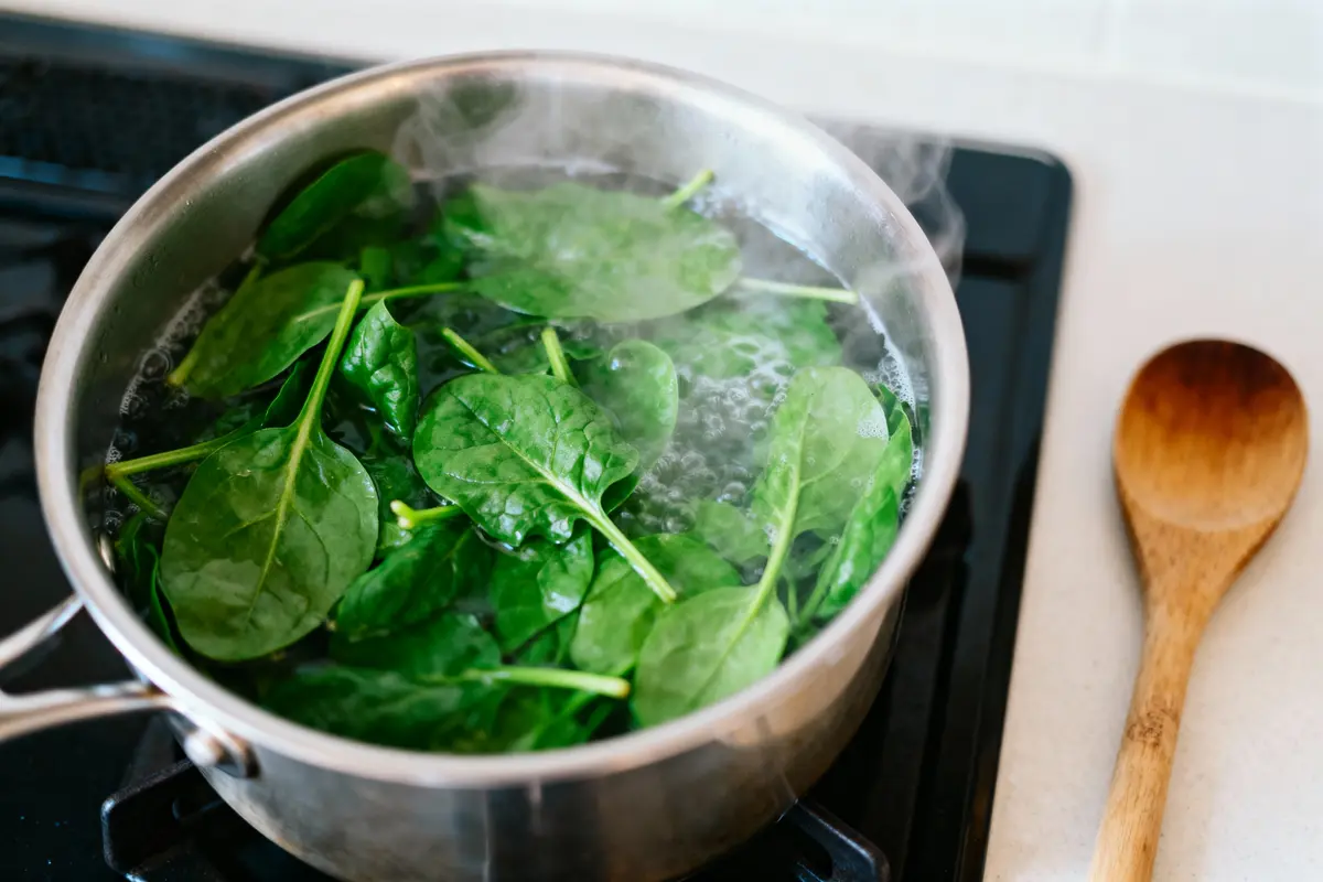 pexels-michal-pech-213601-757318 (1) Des épinards frais cuisent dans une casserole sur une cuisinière, cuillère en bois à côté.