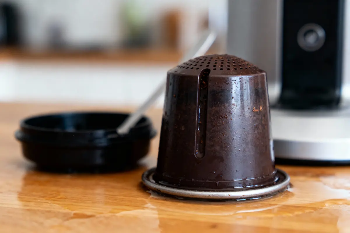 Capsule de café usagée en gros plan, posée sur une table avec de l'eau autour.