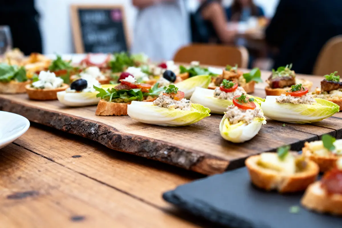 Assortiment de canapés et d'endives garnies sur planche en bois, ambiance de réception conviviale.