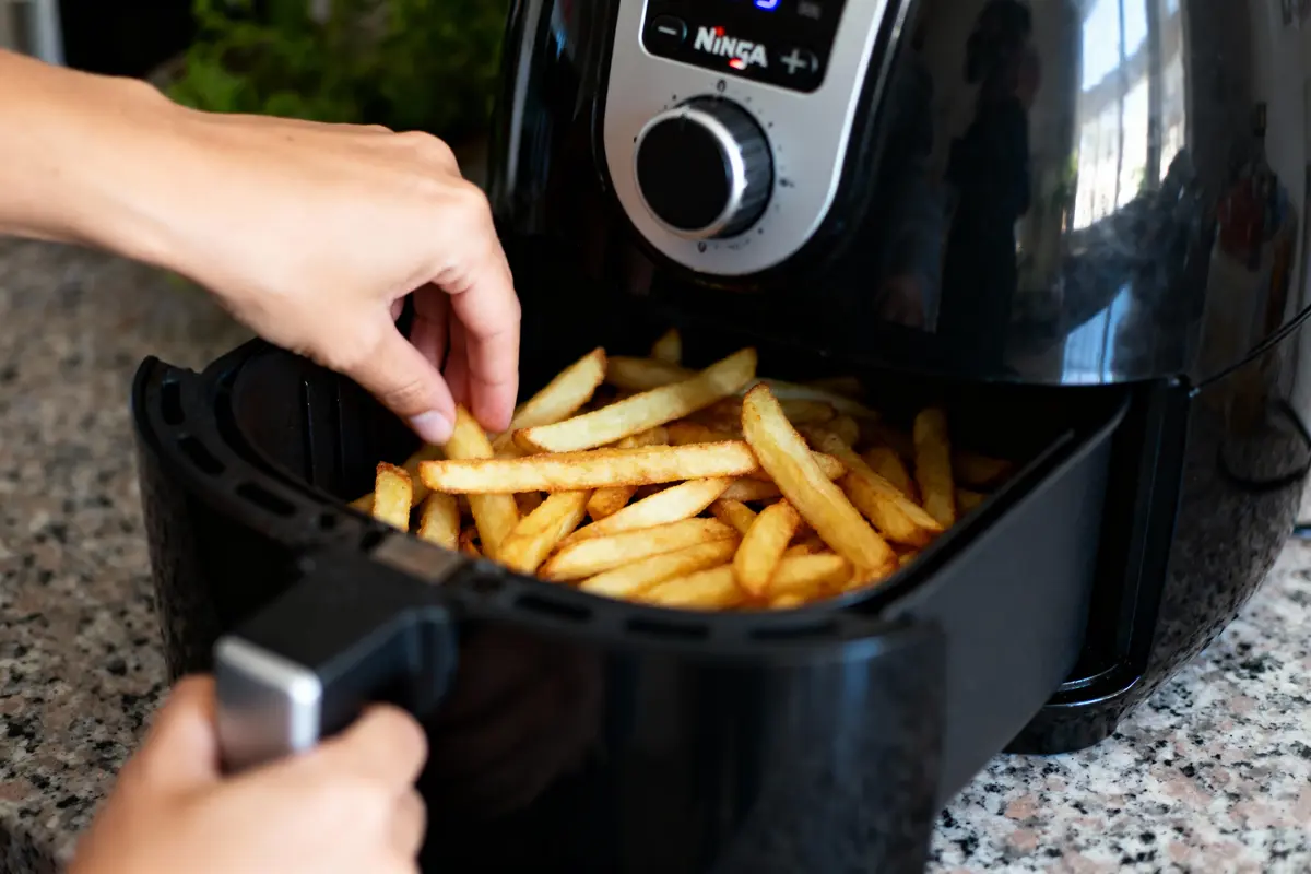 pexels-michal-pech-213601-757318 (1) Main attrapant des frites dorées sortant d'une friteuse à air sur un plan de travail.