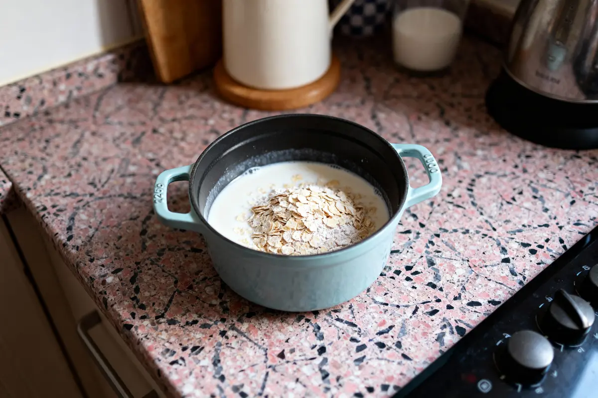 Casserole bleue avec lait et flocons d'avoine sur plan de travail en marbre rose.