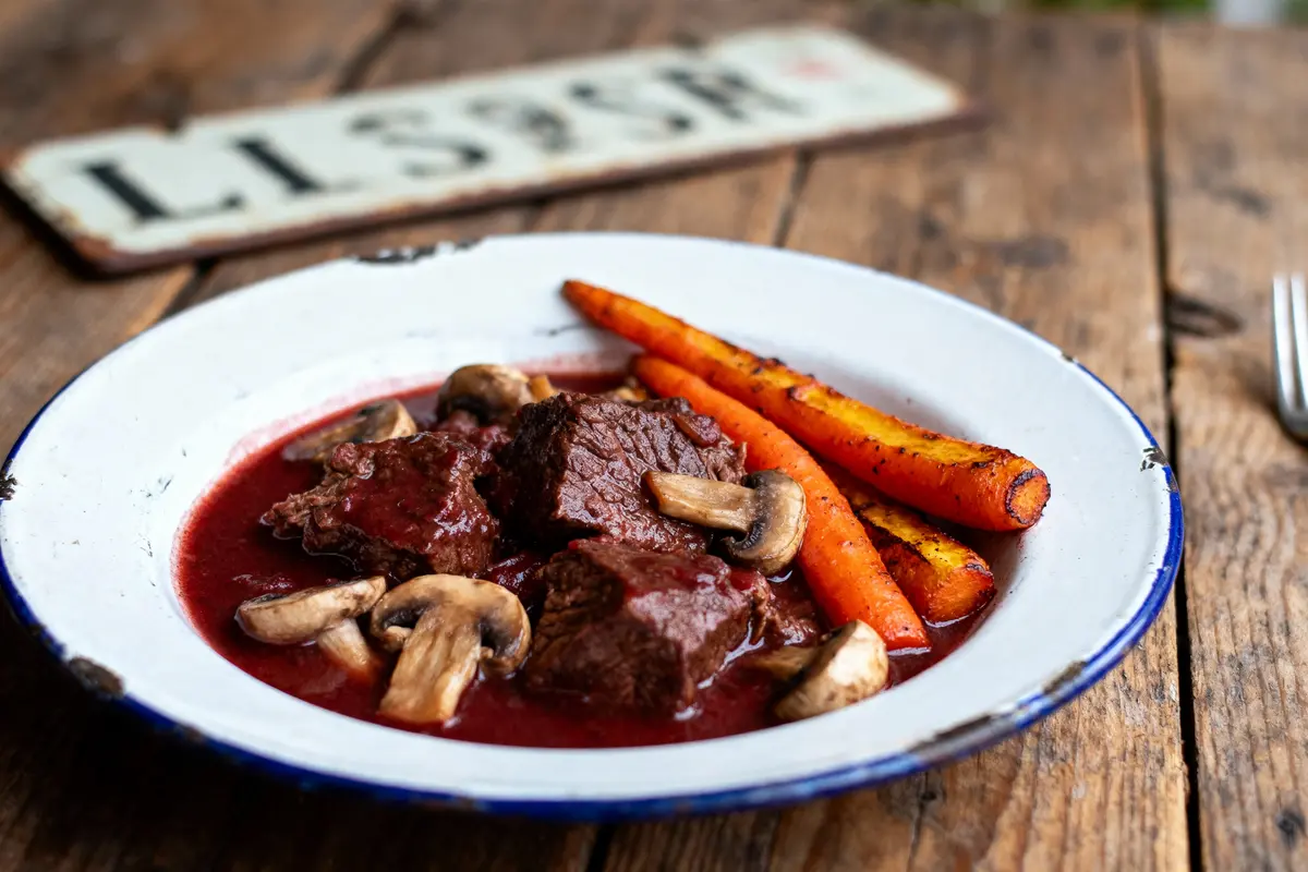 Assiette avec bœuf bourguignon, champignons, carottes grillées, sur table en bois rustique. Plaque en arrière-plan.