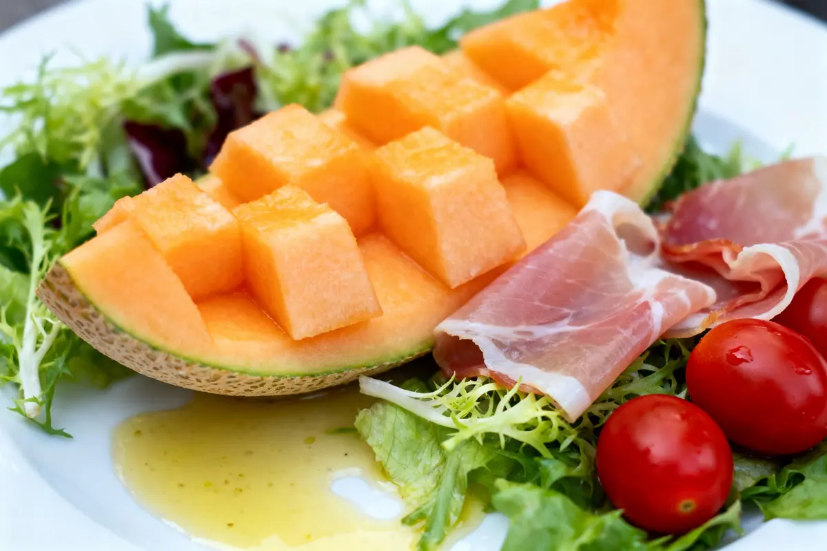 pexels-michal-pech-213601-757318 (1) Demi-melon détaillé, jambon, tomates cerises et salade verte sur une assiette avec vinaigrette.