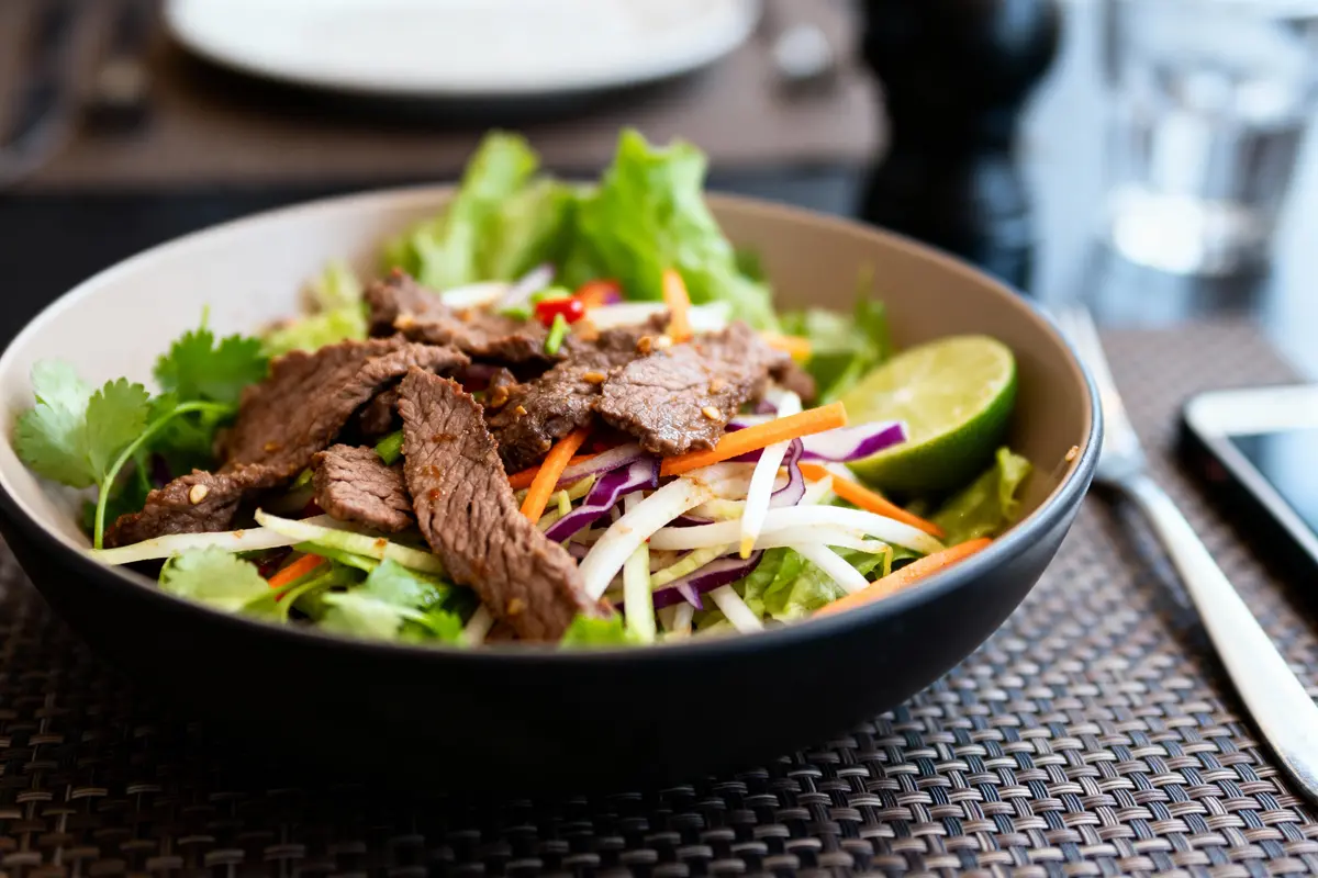 Salade colorée avec bœuf grillé, légumes variés et quartier de citron vert dans un bol.