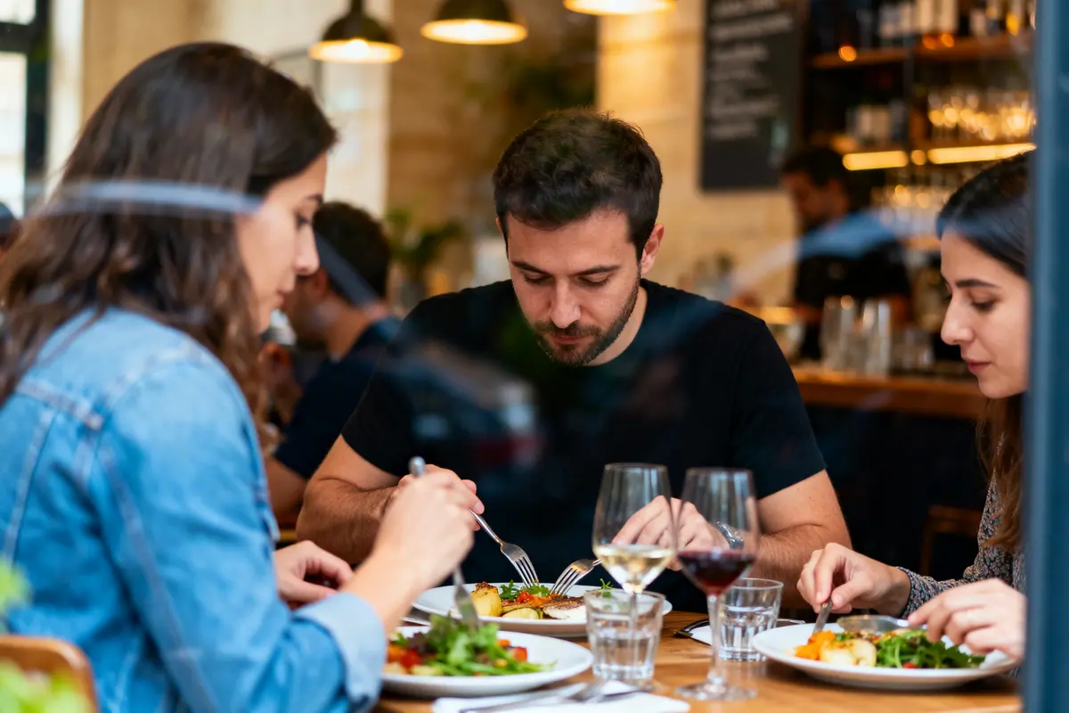 Trois personnes dînent dans un restaurant, dégustant des plats et du vin, ambiance décontractée.
