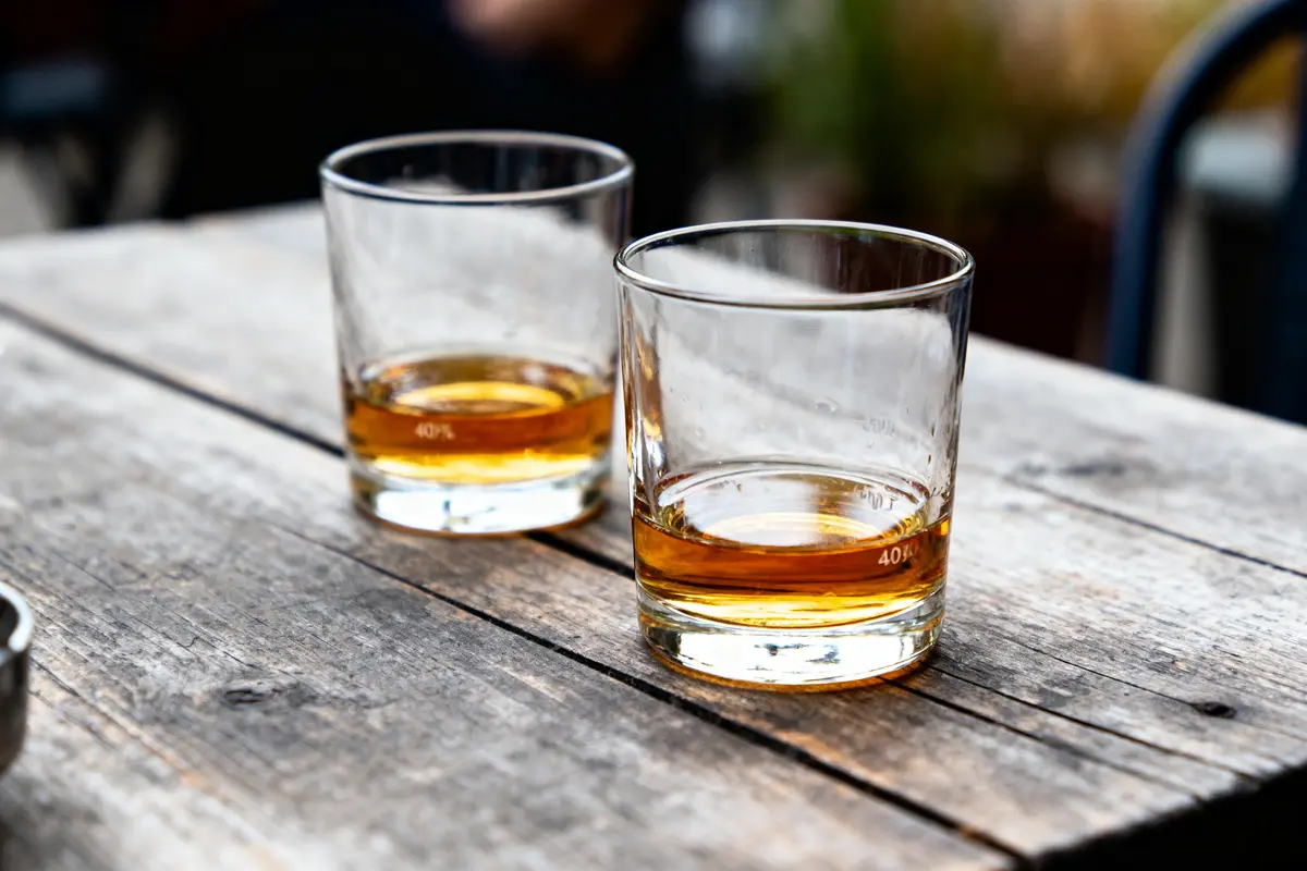 Deux verres de whisky sur une table en bois vieilli, fond flou.