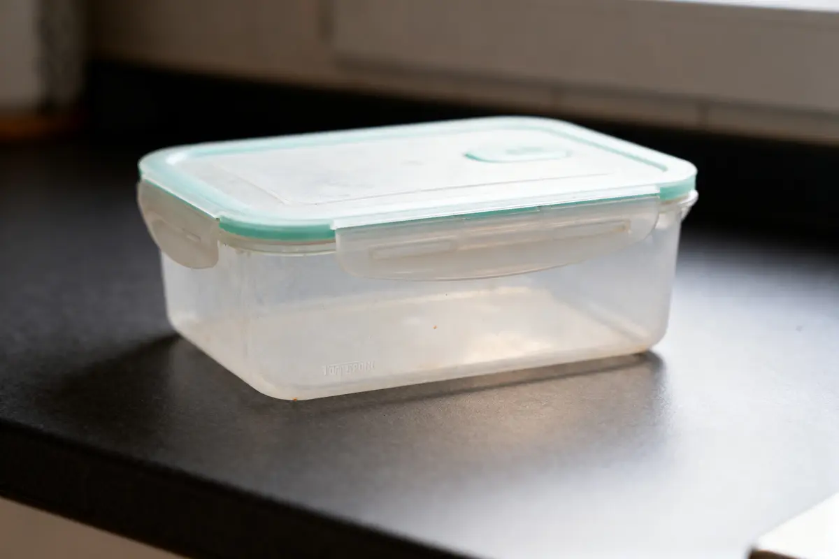 Boîte plastique avec couvercle vert clair, posée sur un plan de travail sombre.