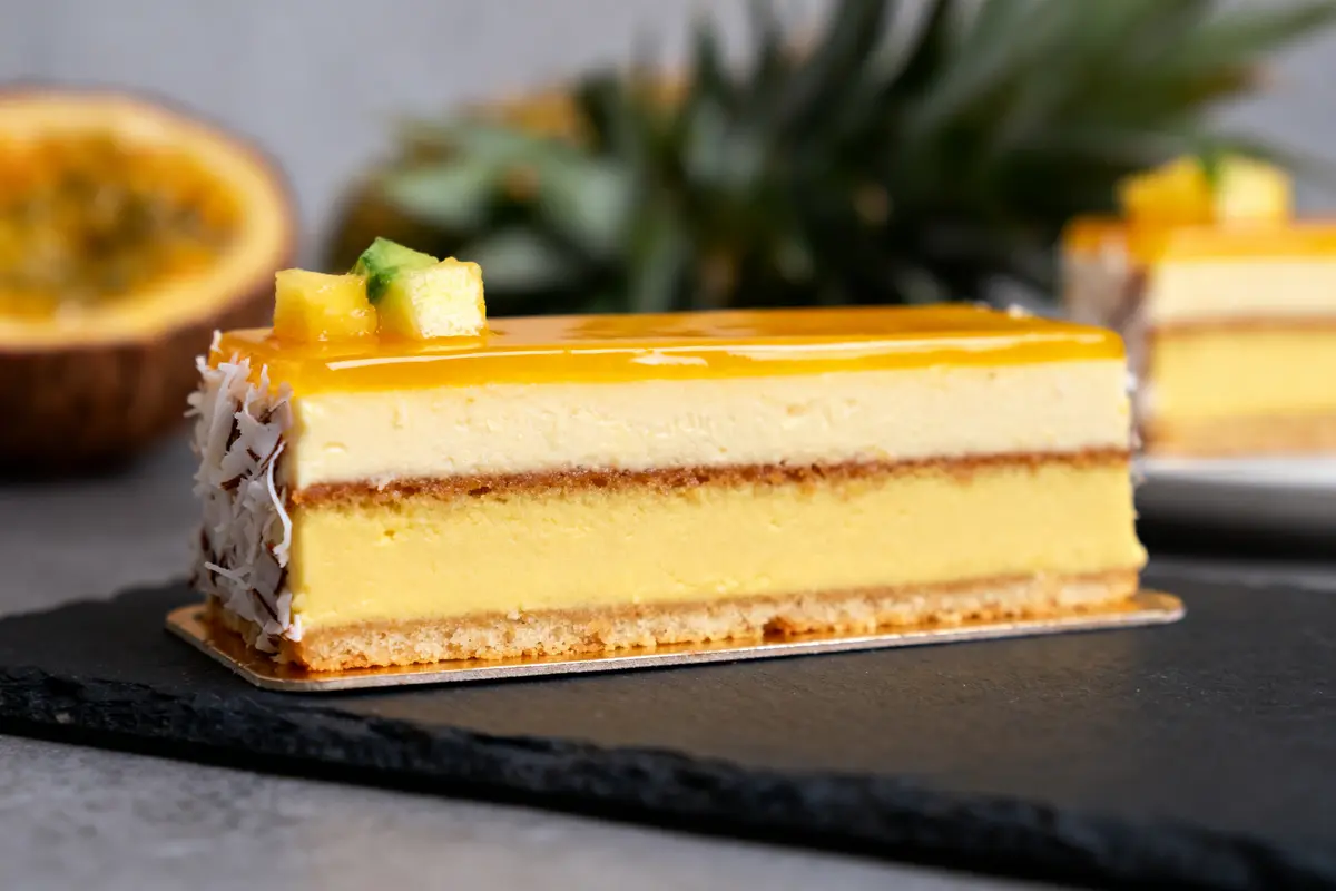Tranche de gâteau tropical avec glaçage jaune et morceaux d'ananas sur ardoise, fond flou.