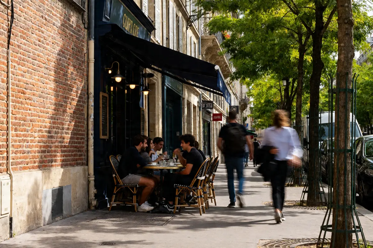 Groupe discutant à une terrasse de café, illustrant les 14 besoins de Virginia Henderson