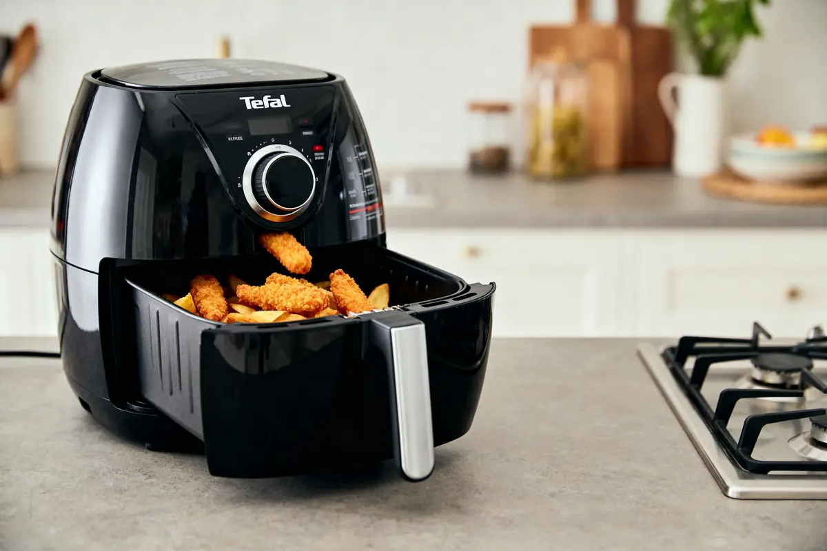 Friteuse à air Tefal avec bâtonnets de poulet et frites, sur un comptoir moderne.