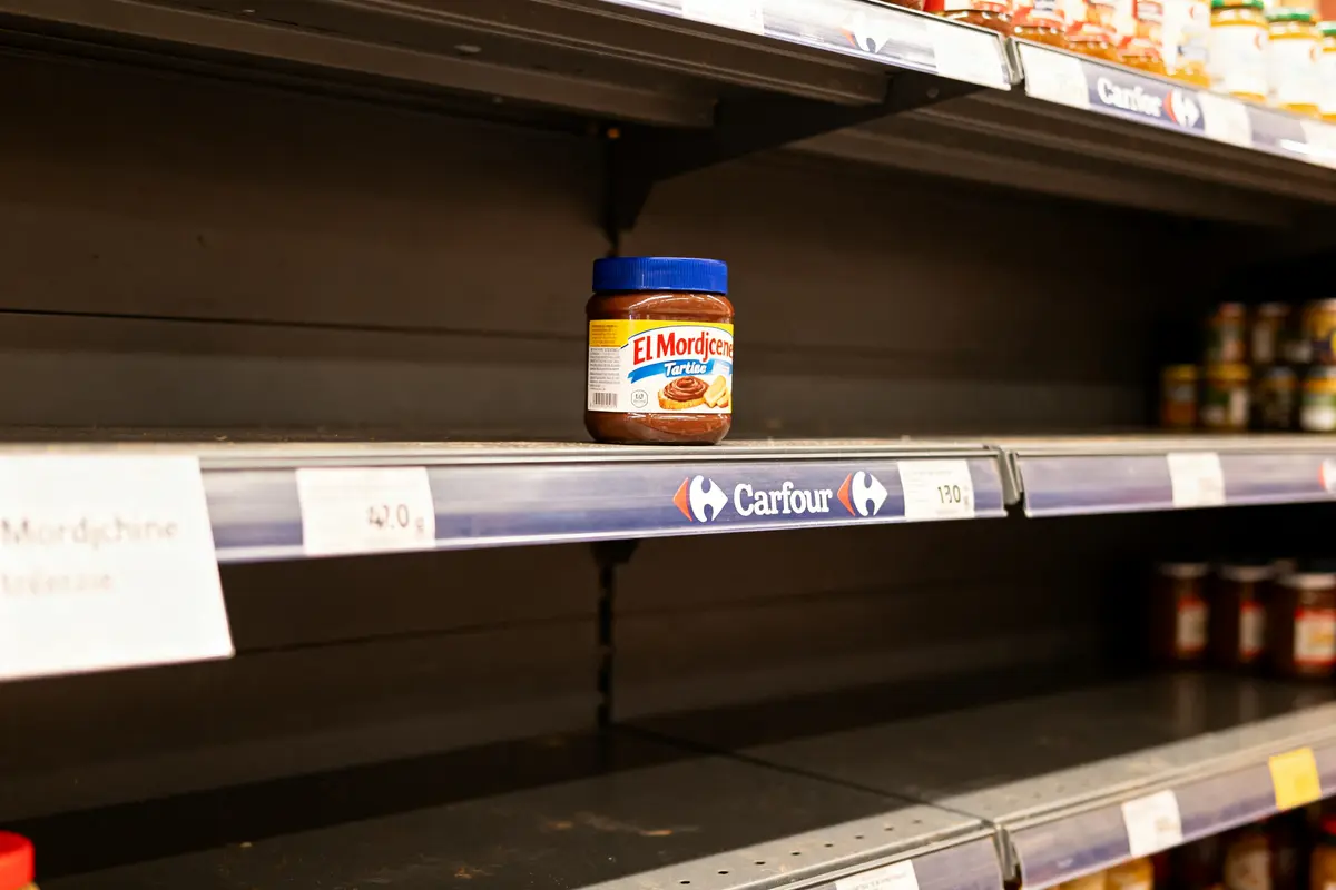 Bocal El Mordjane sur une étagère presque vide, supermarché Carrefour, quelques produits visibles au fond.