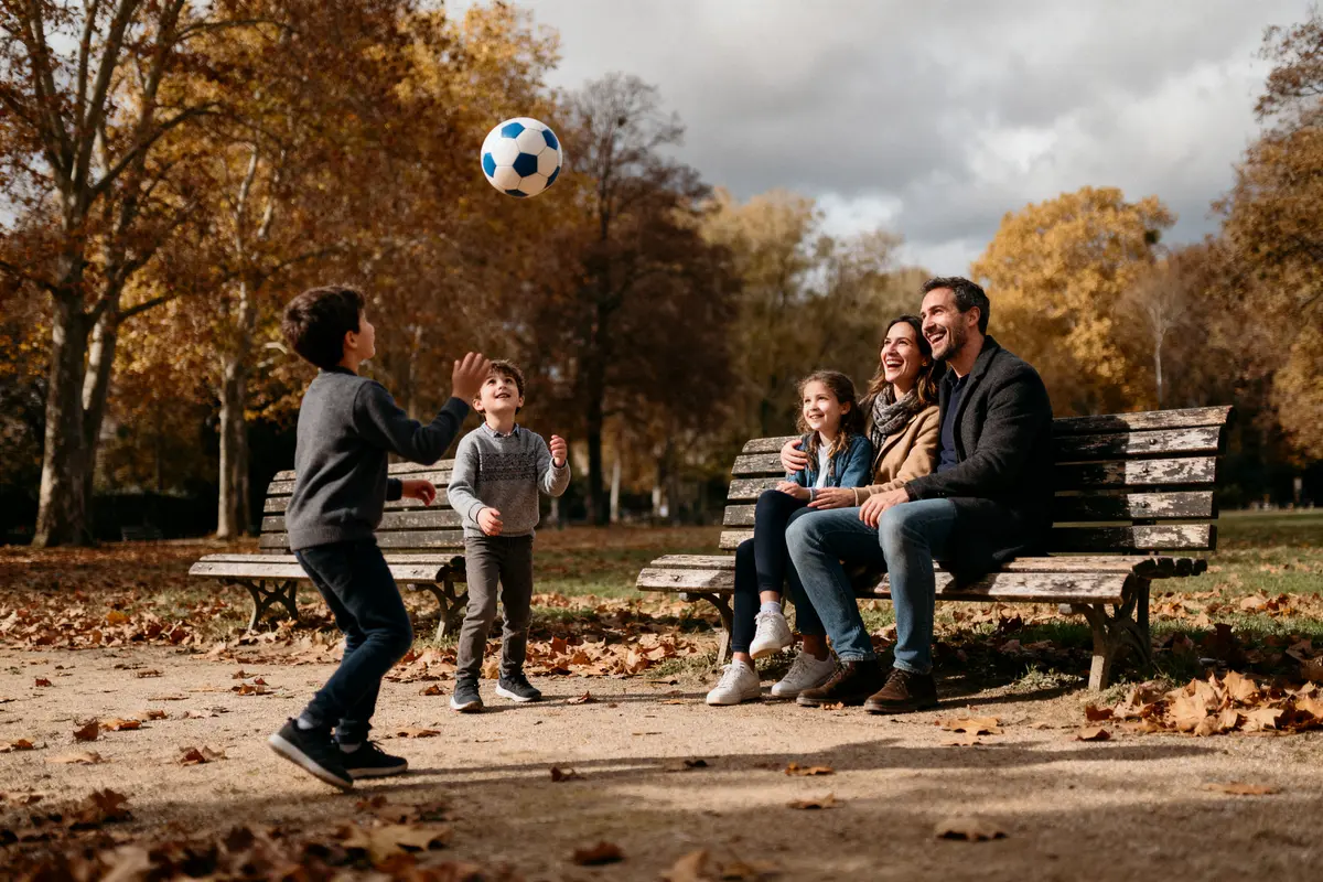 pexels-michal-pech-213601-757318 (1) Famille souriante assise sur un banc, enfants jouant au ballon, parc automnal.