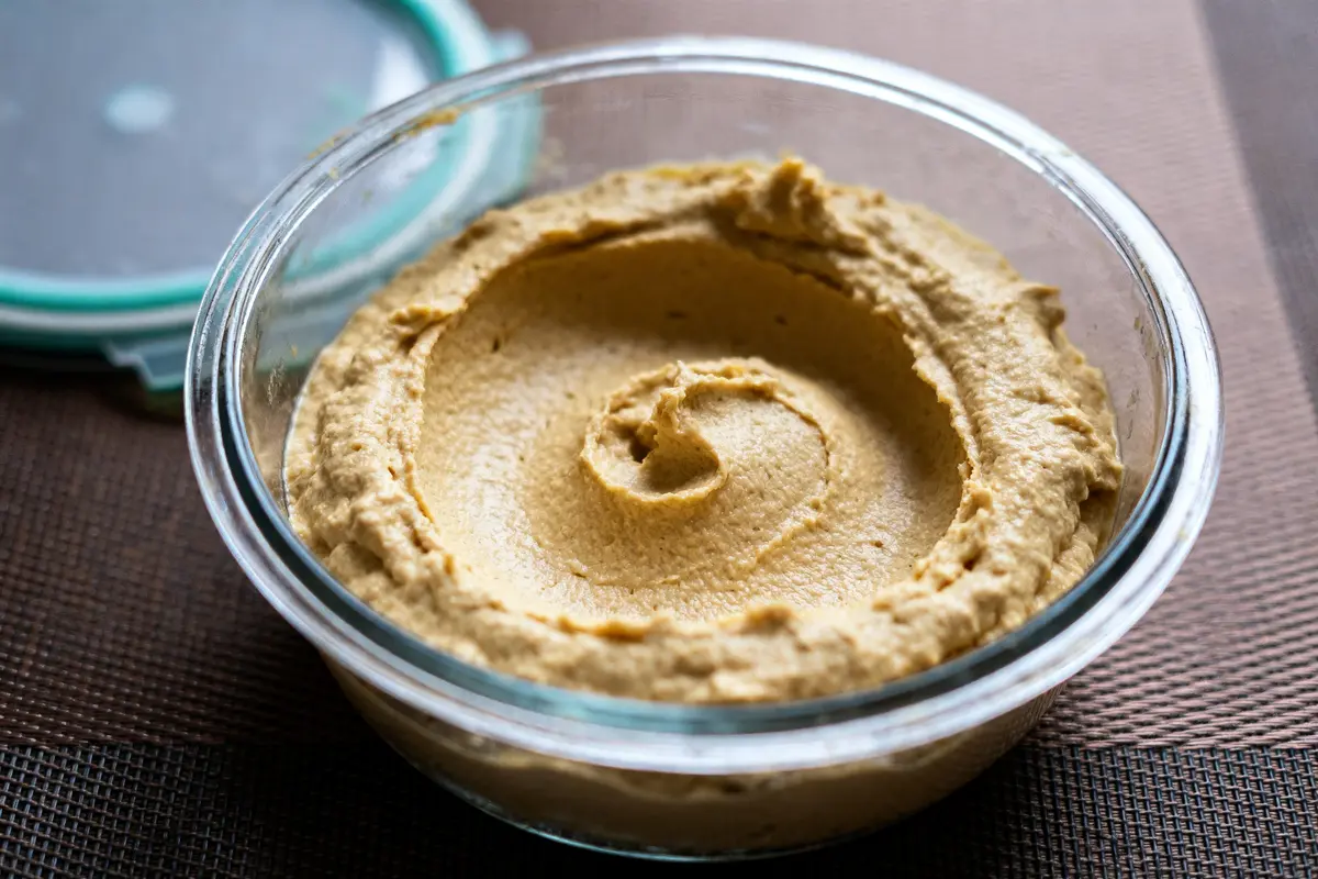 Bol de houmous crémeux dans un récipient en verre, avec couvercle à côté.
