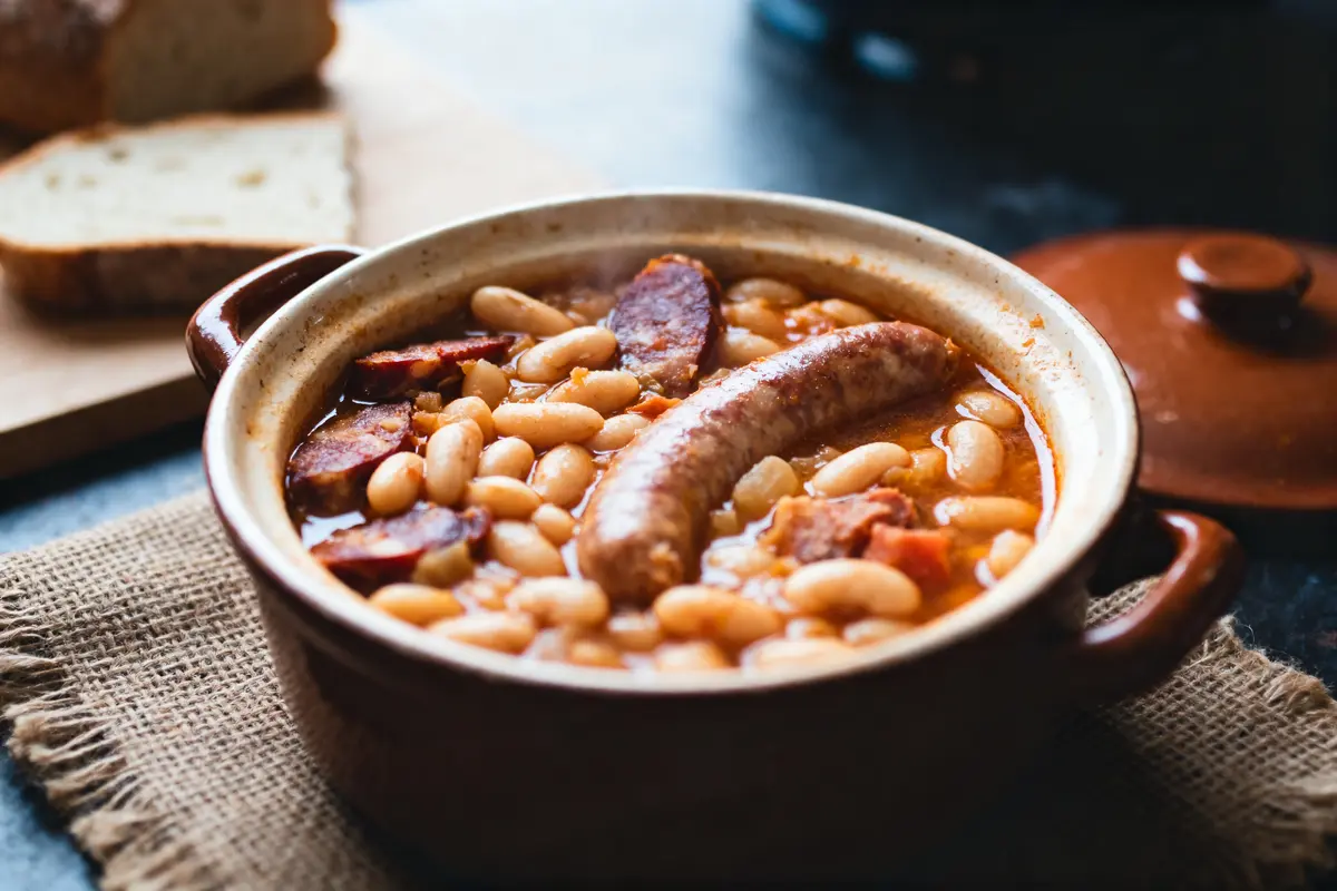Plat de cassoulet avec saucisses et haricots blancs dans une cocotte en céramique, pain en arrière-plan.