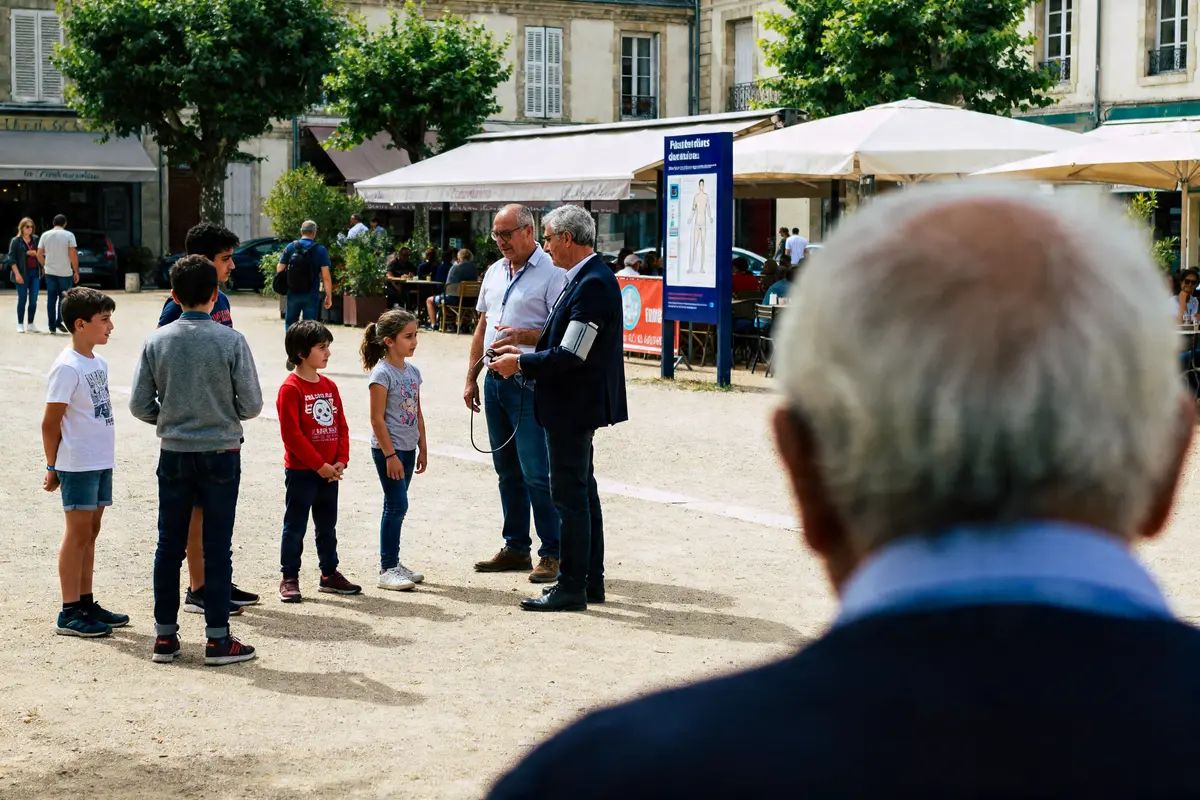 Un groupe d'enfants observe un démonstrateur vérifiant la tension normale sur une place.