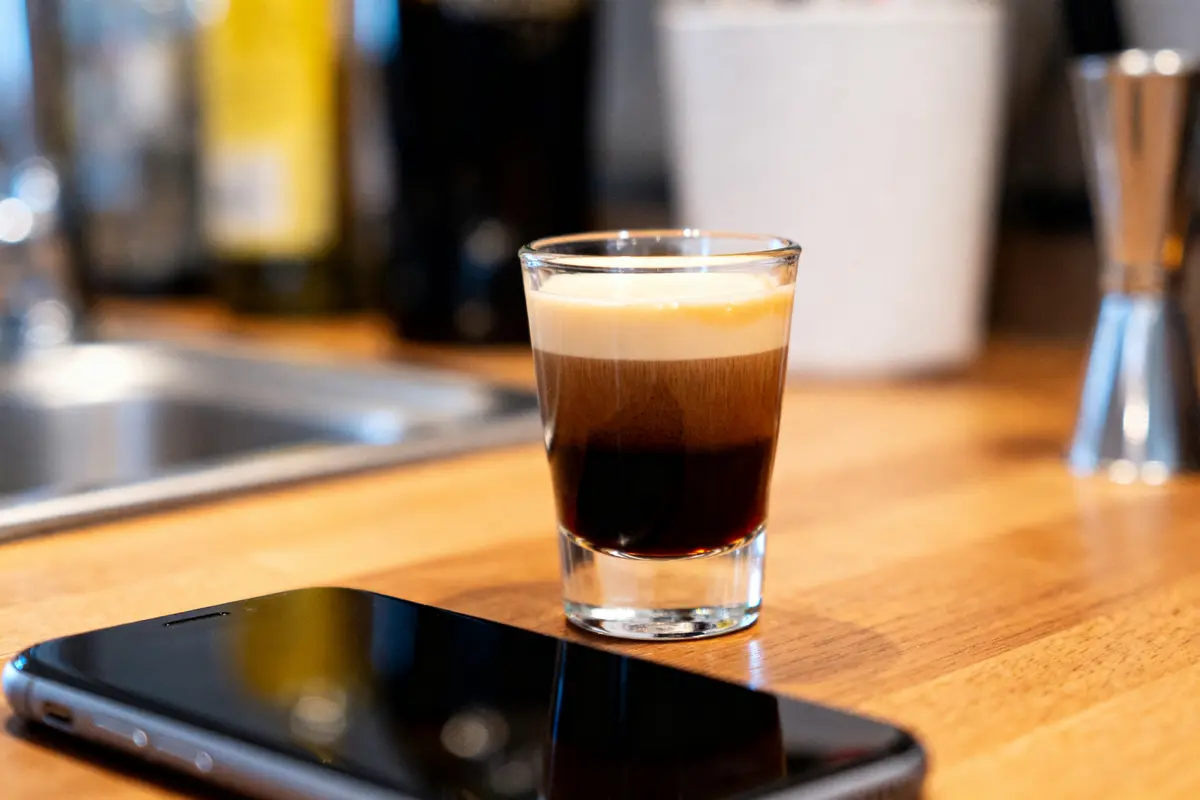 Verre de mini cocktail Guinness posé sur comptoir en bois près d'un téléphone