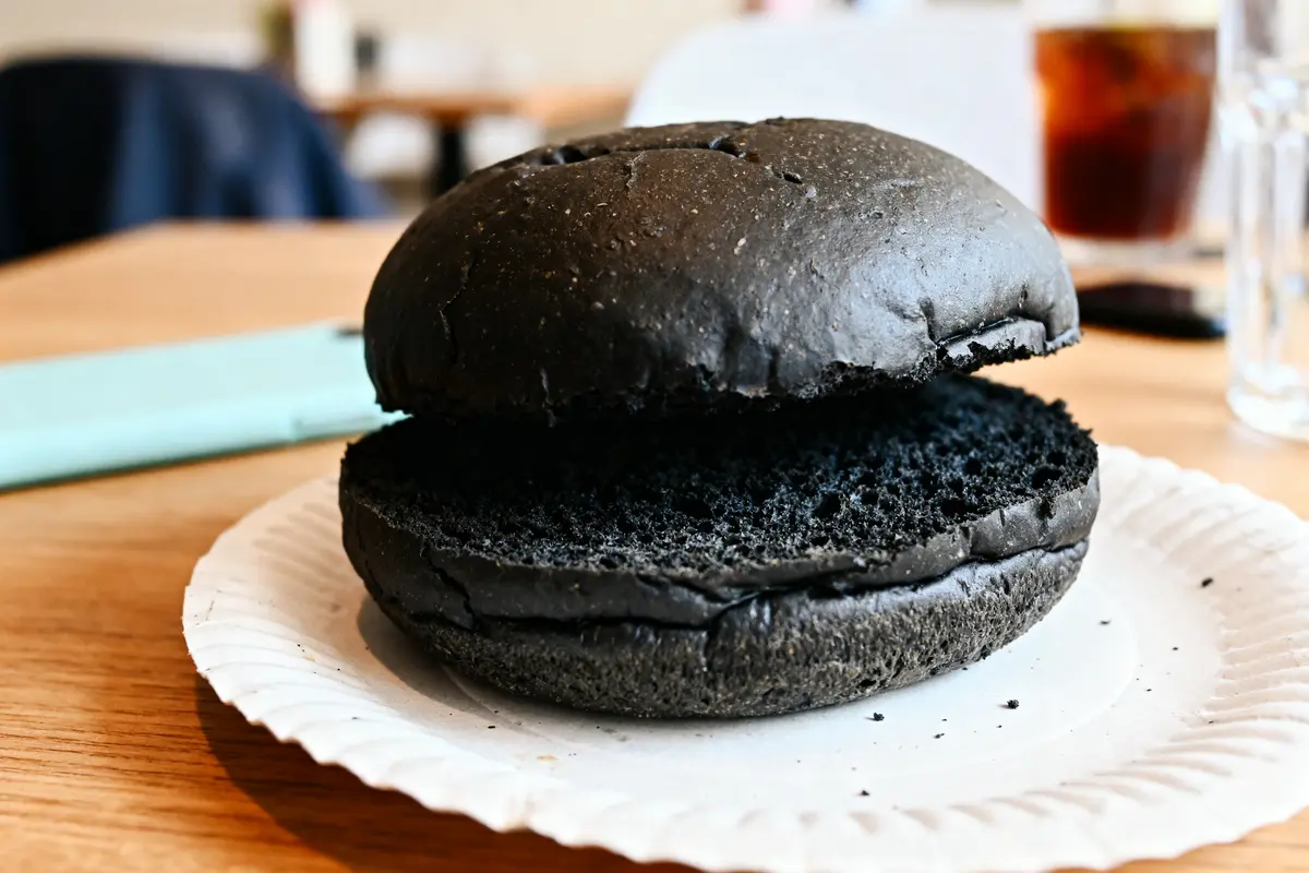 Pain burger noir posé sur une assiette blanche en gros plan sur une table en bois