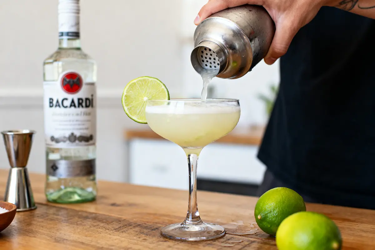 pexels-michal-pech-213601-757318 (1) Verre de cocktail daïquiri avec lime et bouteille pour recettes de daïquiri sur table bois